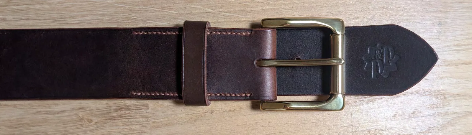 Ceinture en cuir chocolat à boucle laiton, posée sur un plan de travail en bois